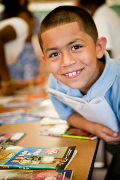 A smiling student reading a book at a school table